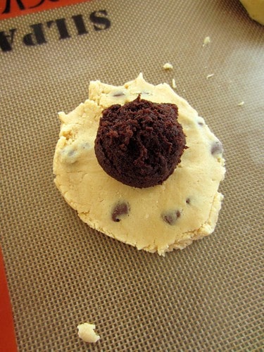 A chocolate cake ball on top of a flattened circle of chocolate chip cookie dough