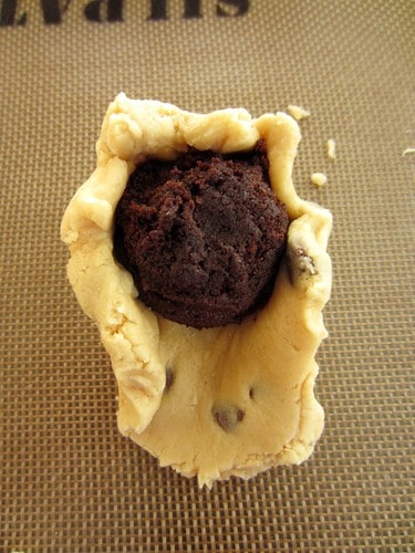 Chocolate chip cookie dough being wrapped around a chocolate cake ball