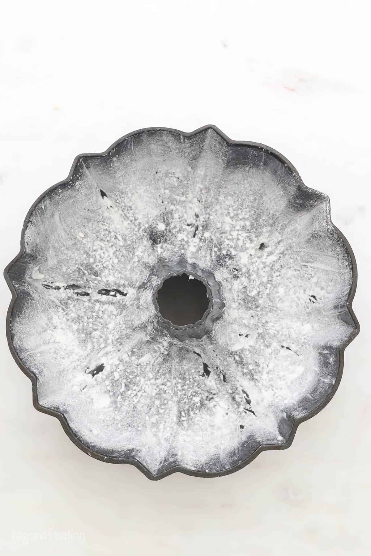 A greased and floured bundt cake pan on a white countertop