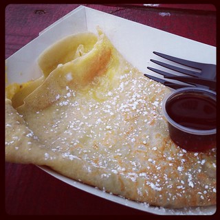 A French Toast Crepe in a paper boat with a cup of maple syrup
