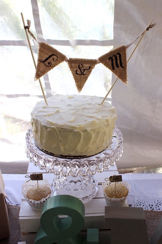 Homemade wedding cake on a clear glass stand with L&M flag on top