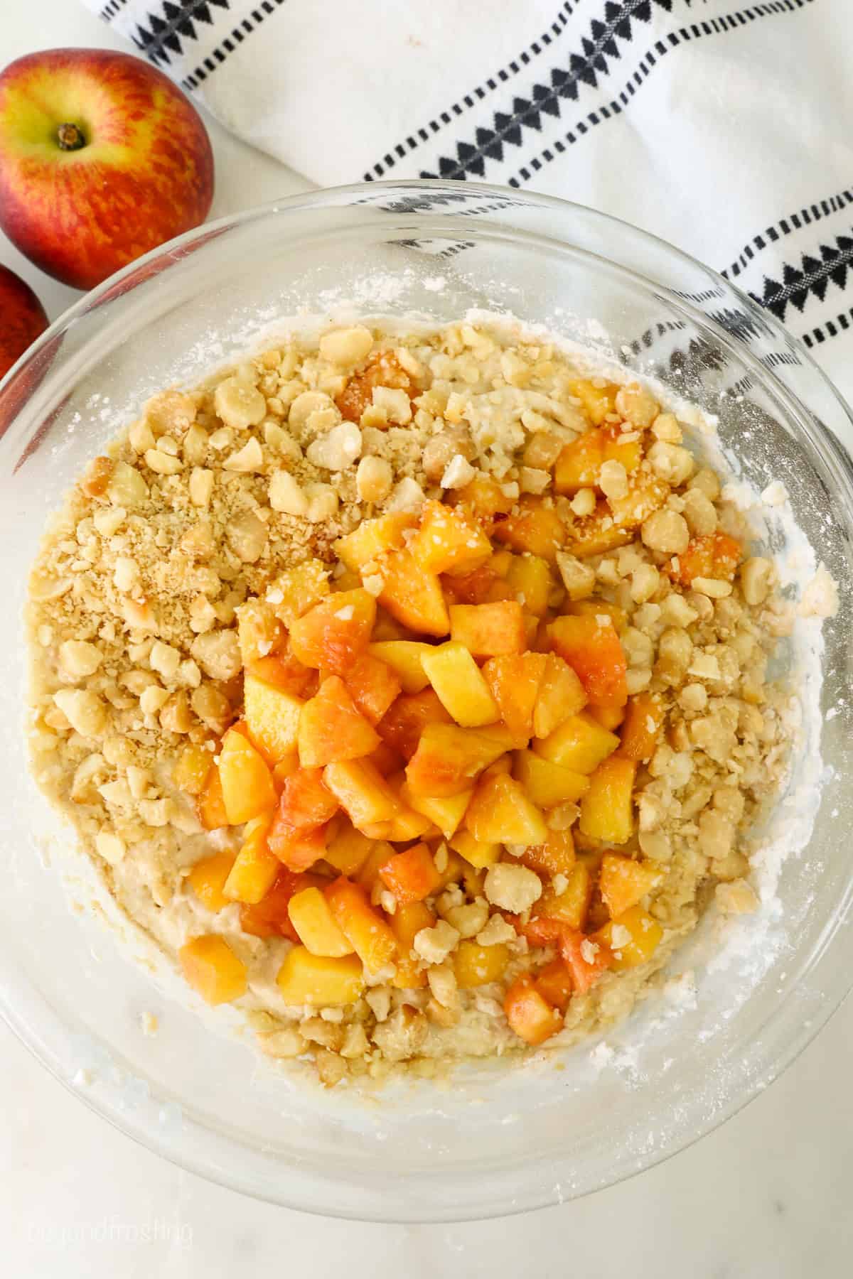 Peaches and macadamia nuts added to muffin batter in a glass mixing bowl.