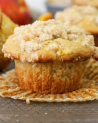 A peach macadamia nut muffin in an unwrapped muffin liner, with more muffins in the background.