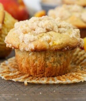 A peach macadamia nut muffin in an unwrapped muffin liner, with more muffins in the background.