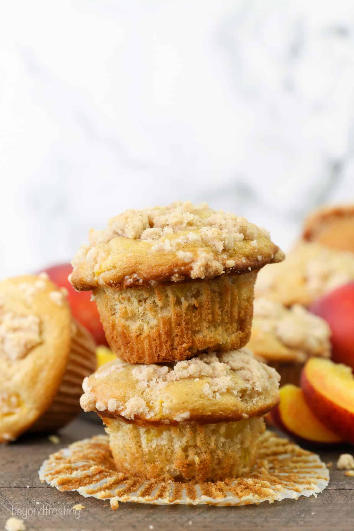 Two peach macadamia nut muffins stacked on top of one another with more muffins in the background.