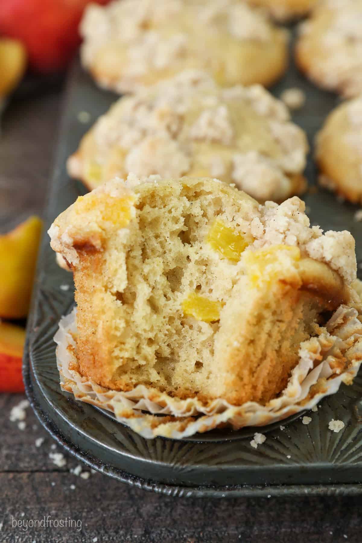 A peach macadamia nut muffin with a bite missing resting in the well of a muffin tin, with more muffins in the background.