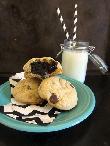 A platter of Cake Ball Stuffed Cookies on a plate with a napkin. One cookie is cut in half so you can see the rich, dense chocolate inside.