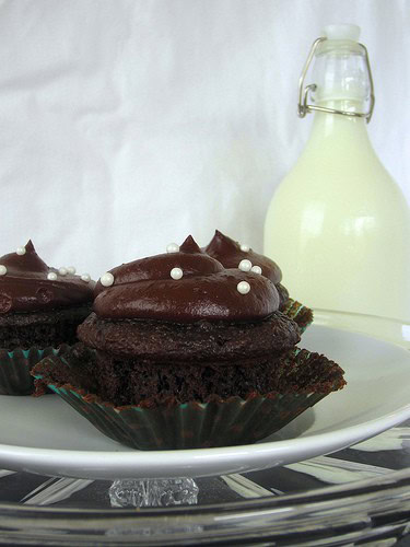 A chocolate cream cheese cupcake topped with rich Hershey's Chocolate Frosting in front of a jug of milk.