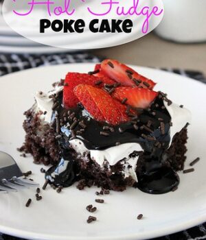 A slice of Hot Fudge Poke Cake topped with chocolate sauce and strawberries.