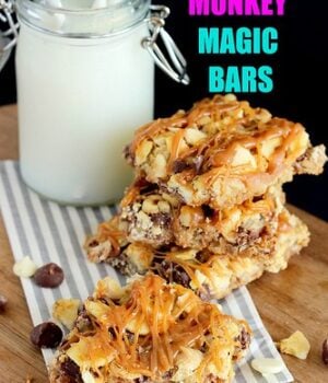 Stacked Chunky Monkey Magic Bar Squares with chocolate chips, banana chips, and walnuts topped with a caramel drizzle resting in front of a glass of milk.