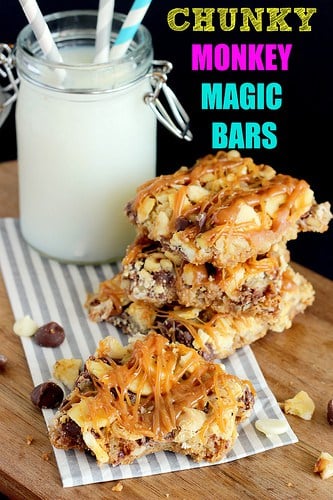 Stacked Chunky Monkey Magic Bar Squares with chocolate chips, banana chips, and walnuts topped with a caramel drizzle resting in front of a glass of milk.