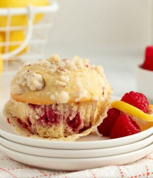 An almond raspberry muffin partially unwrapped from a muffin liner on a plate next to fresh rasbperries.