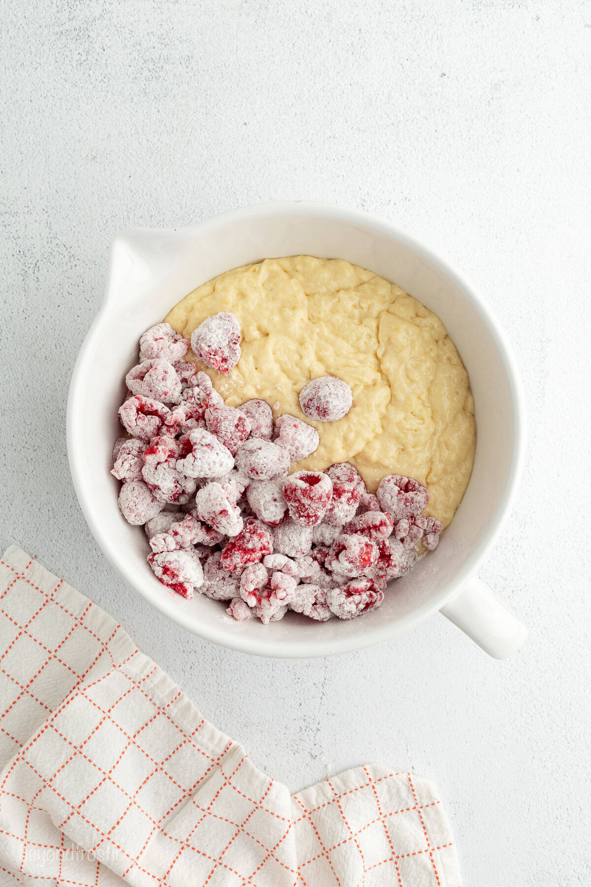 Flour-coated raspberries being added to muffin batter in a bowl.