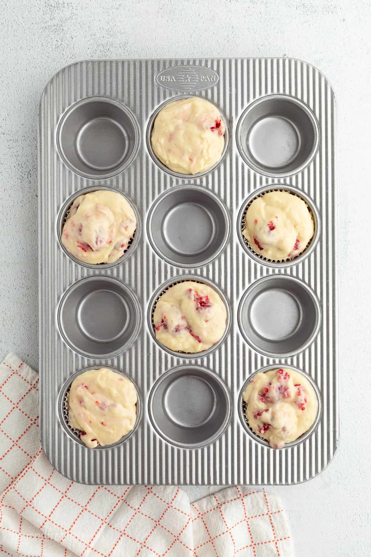 Overhead view of a muffin tin with every other well filled with raspberry muffin batter.