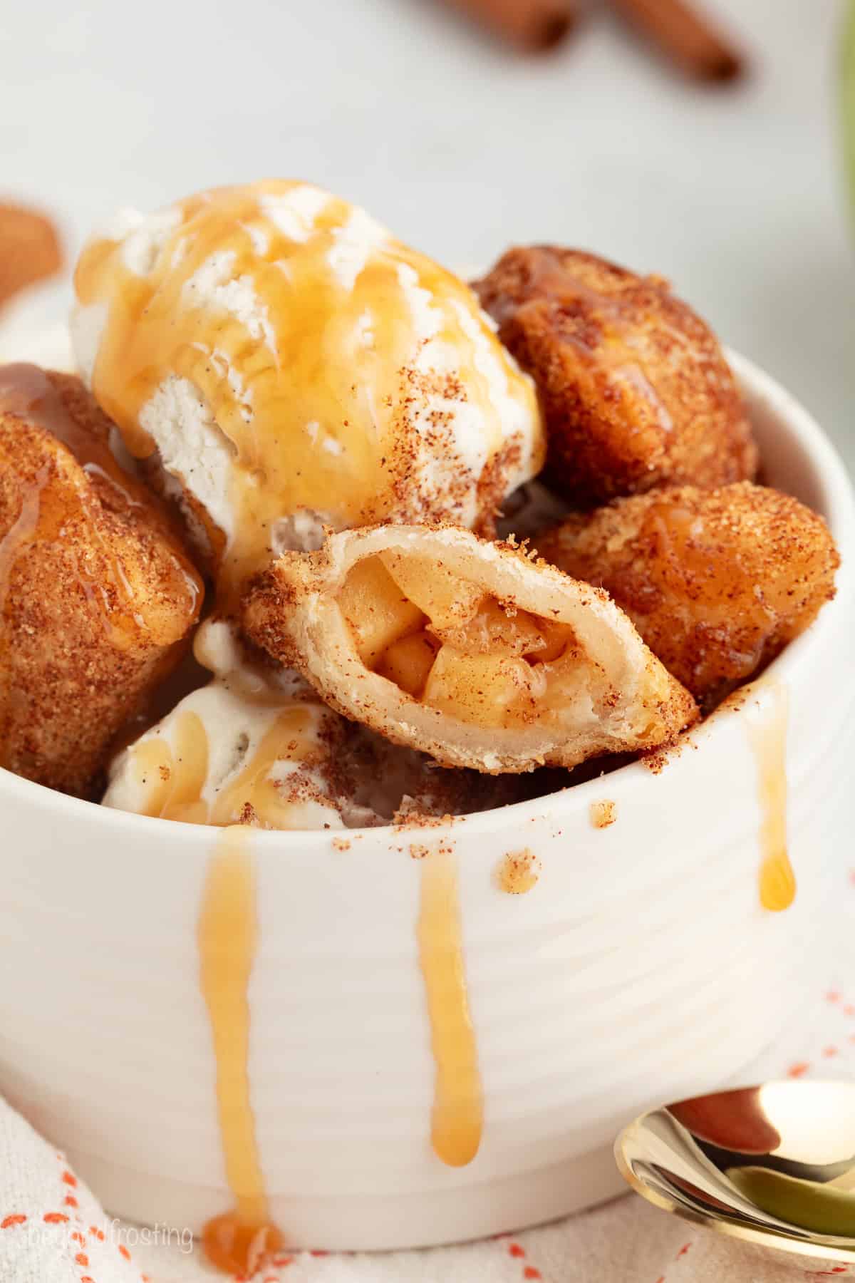 Golden-fried apple pie bites are easy to make, with refrigerated pie dough and gooey homemade apple pie filling. Like bite-sized apple pies! A bowl of fried apple pie bites topped with ice cream and drizzled with caramel sauce.