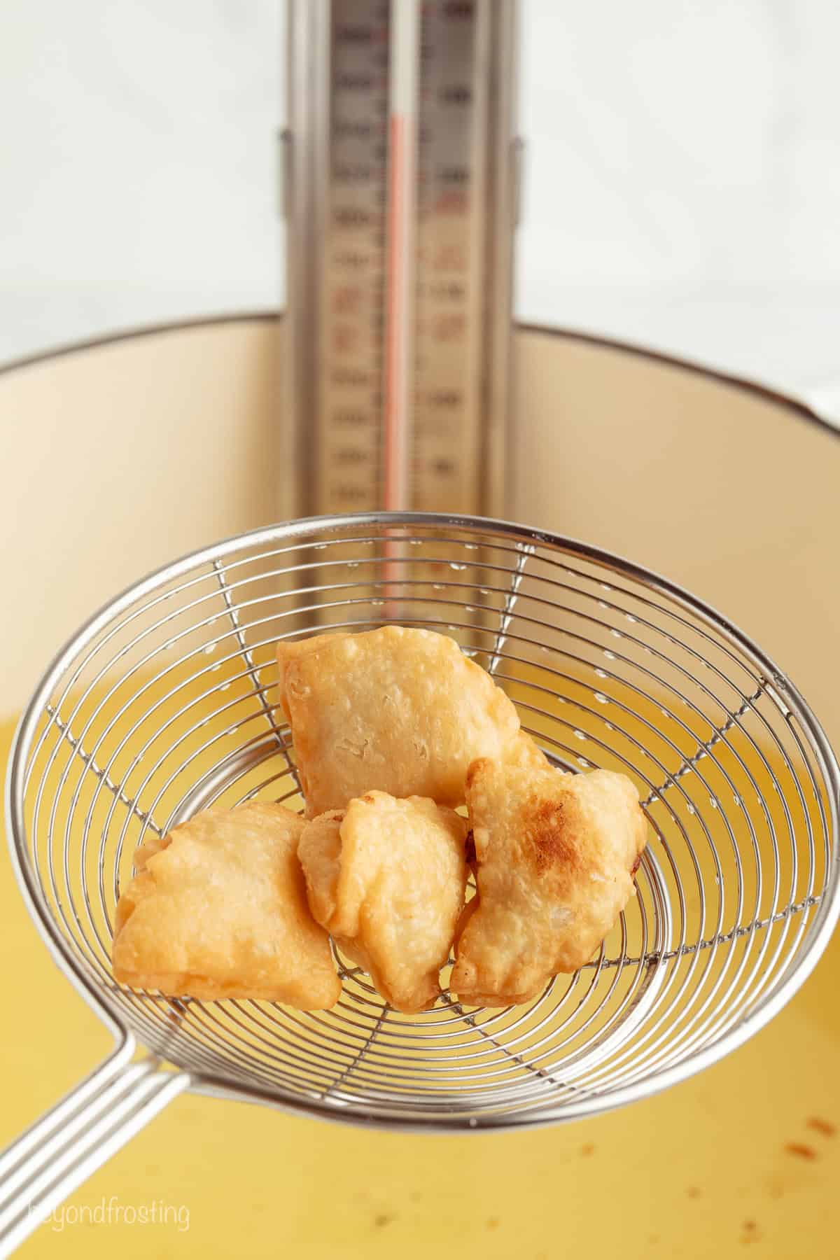 Golden-fried apple pie bites are easy to make, with refrigerated pie dough and gooey homemade apple pie filling. Like bite-sized apple pies! Lifting deep fried apple pie bites from a pot of hot oil with a slotted spoon.