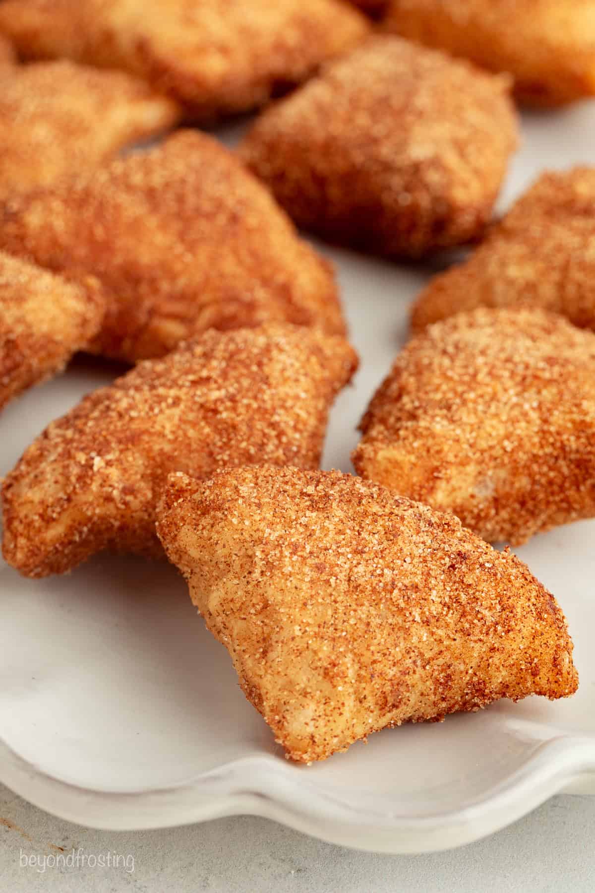 Close up of crispy apple pie bites coated with cinnamon sugar on a plate.