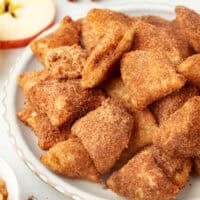 Golden-fried apple pie bites coated with cinnamon sugar on a plate.
