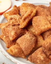 Golden-fried apple pie bites coated with cinnamon sugar on a plate.