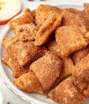 Golden-fried apple pie bites coated with cinnamon sugar on a plate.