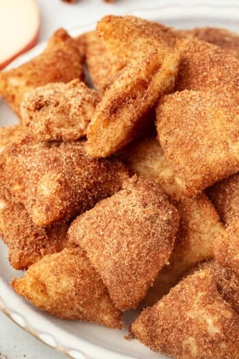 Golden-fried apple pie bites coated with cinnamon sugar on a plate.