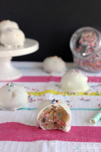 White chocolate coated cake batter cookie dough truffles on a striped cloth with a bite out of one