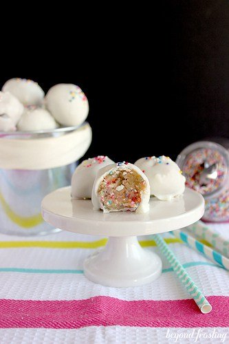 White chocolate coated cake batter cookie dough truffles on a cake stand with a bite out of one