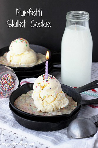 A Funfetti Skillet Cookie in a pan with a glass of milk in the background topped with vanilla ice cream and a candle.