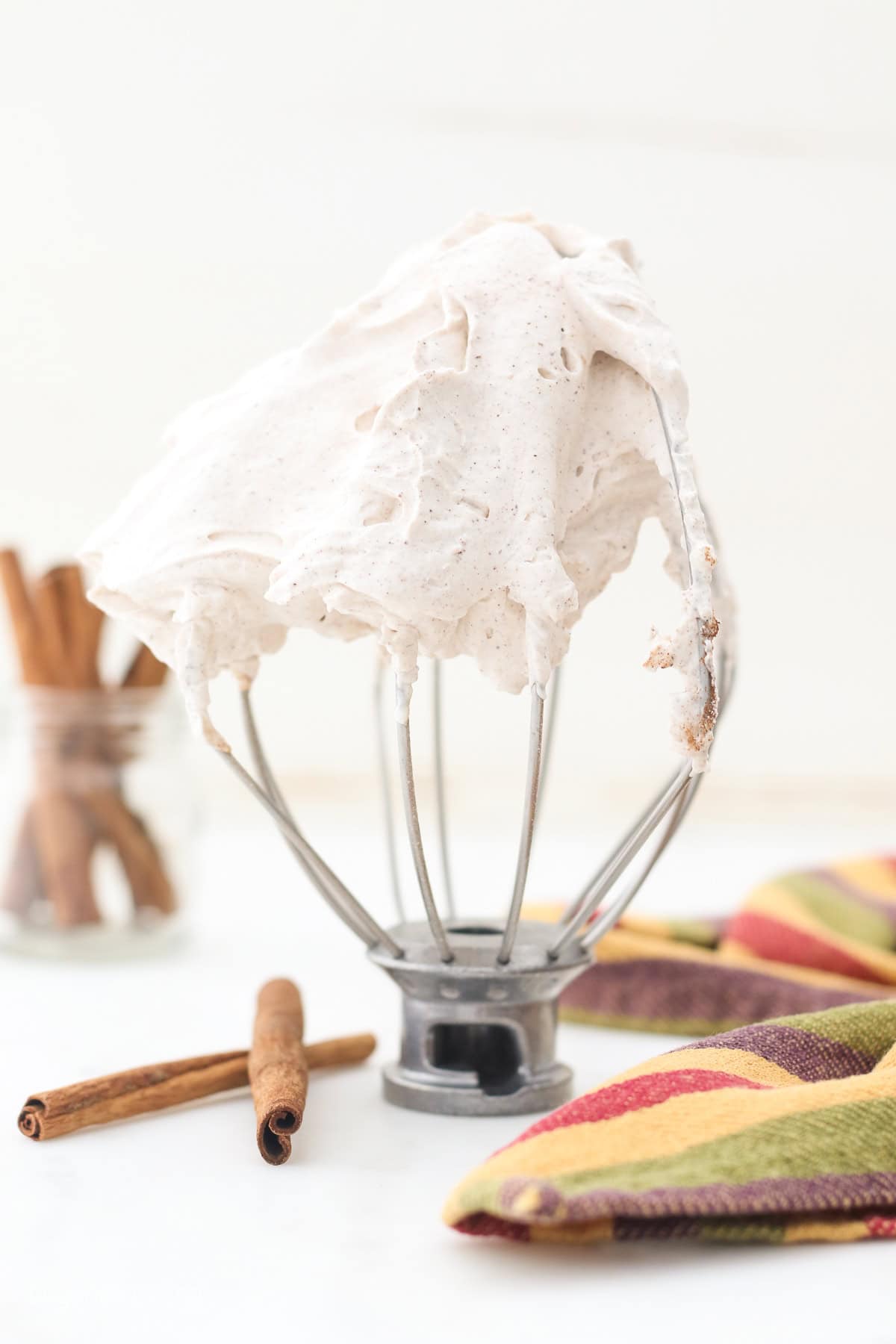 Cinnamon maple whipped cream is the perfect easy fall dessert topping! It's ready in minutes, flavored with warm spice and real maple syrup. Cinnamon maple whipped cream holding stiff peaks on the tip of an upright whisk attachment.