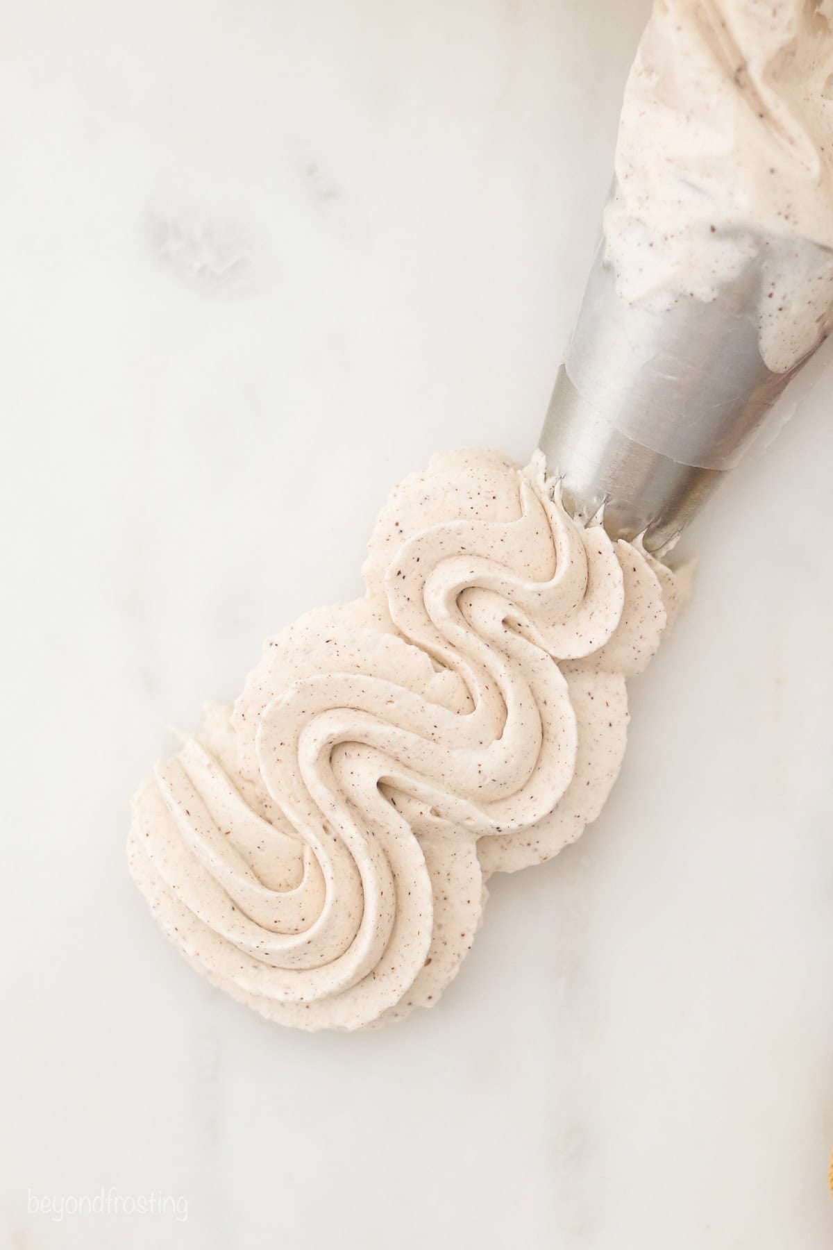 Cinnamon maple whipped cream is the perfect easy fall dessert topping! It's ready in minutes, flavored with warm spice and real maple syrup. Homemade cinnamon maple whipped cream being piped in a squiggle.