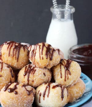 A tray of stacked Cookie Dough Stuffed Donut Holes drizzled with chocolate