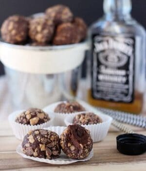 A few Chocolate Whiskey Toffee Truffles in white wrapping in front of a whiskey bottle.