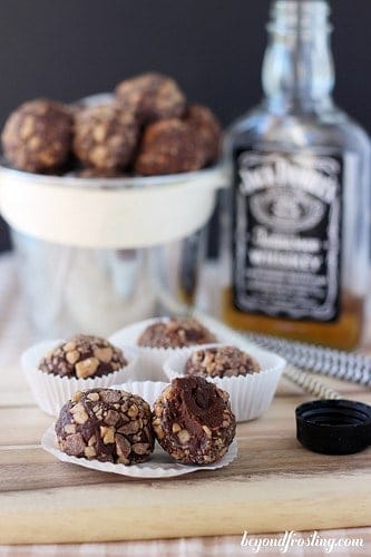 A few Chocolate Whiskey Toffee Truffles in white wrapping in front of a whiskey bottle.