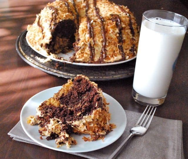 A Slice of Samoa Cake with a Glass of Milk and the Full Cake on a Platter