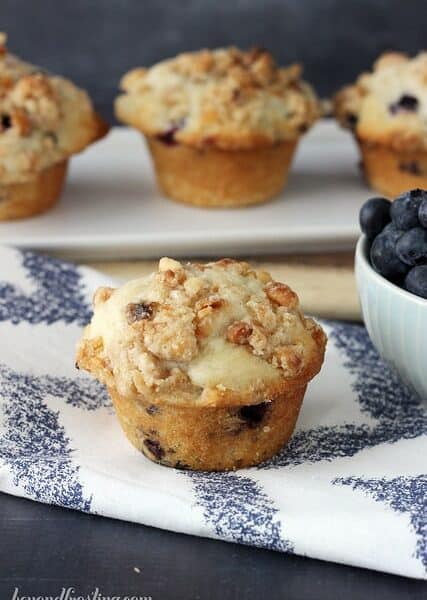 A close up of a Coconut Blueberry Muffin sitting next to a bowl of fresh blueberries