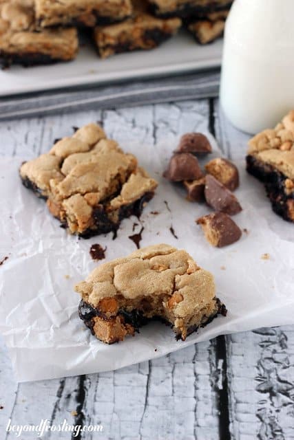 Two Butterfinger Brookie Bars with butterfinger pieces on parchment with a bite removed from one bar