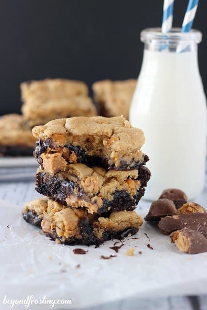 Butterfinger Brookie bars stacked next to a glass of milk with a bite out of the top bar