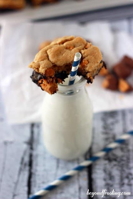 A Butterfinger Brookie Bar with a bite removed sitting on top of a glass of milk with a straw