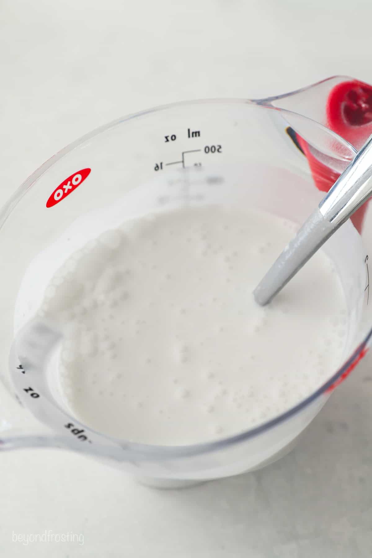 Stirred coconut milk in a measuring cup with a spoon.