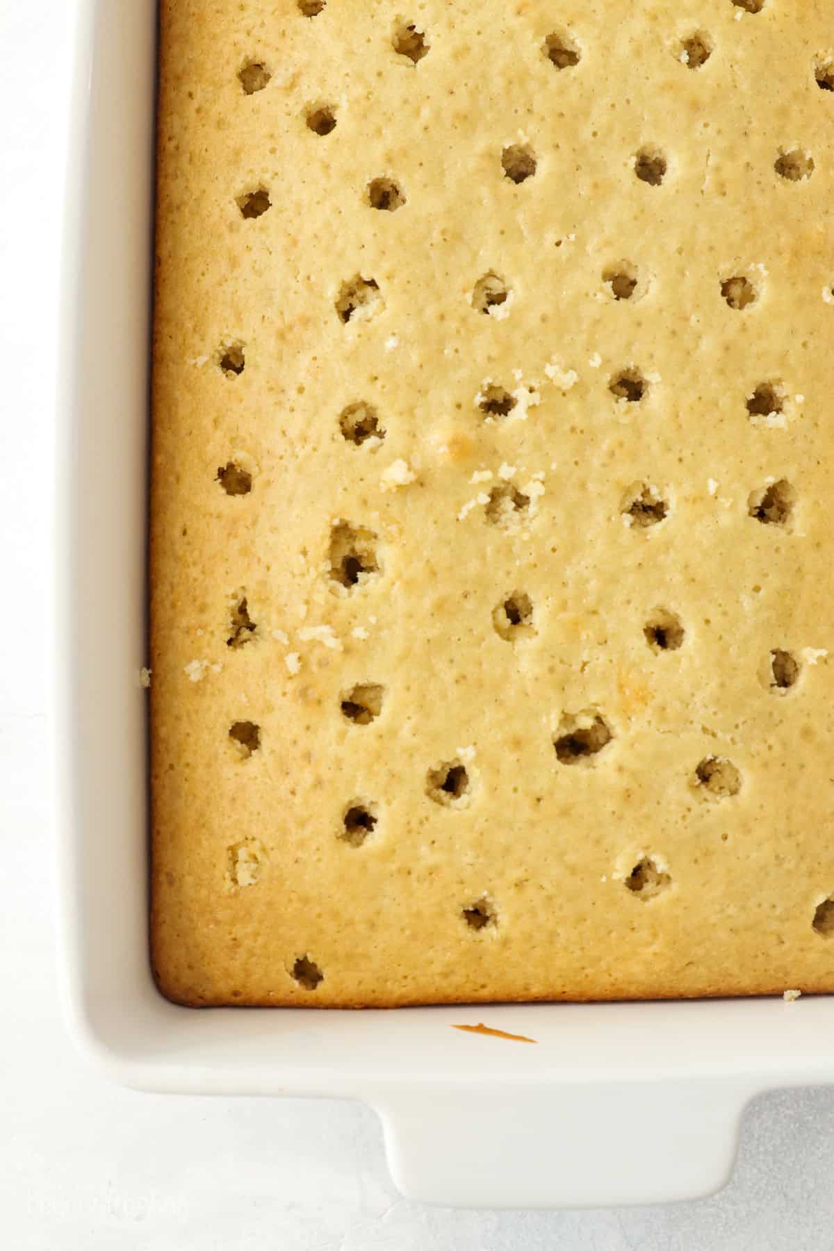 Overhead view of a baked coconut cake with holes poked in the top.