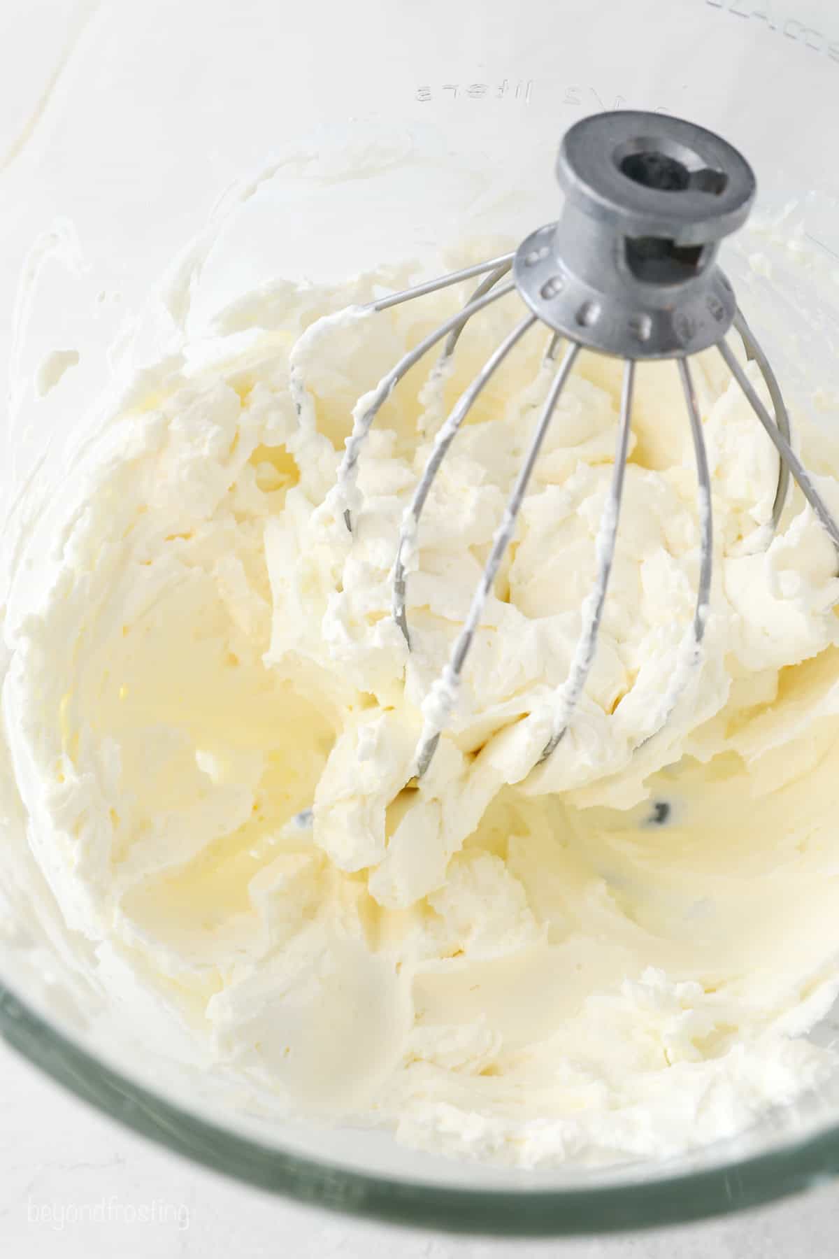Whipped cream cheese frosting in a glass bowl with a whisk attachment.