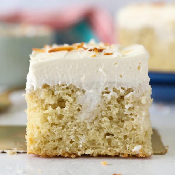 Side view of a slice of frosted coconut poke cake topped with toasted coconut.