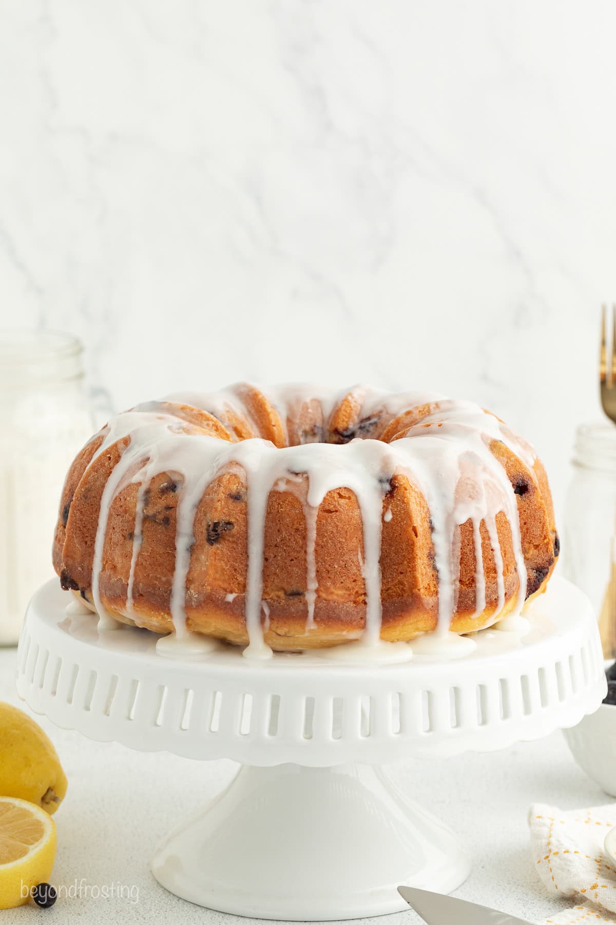 Glazed lemon blueberry bundt cake on a white cake stand.