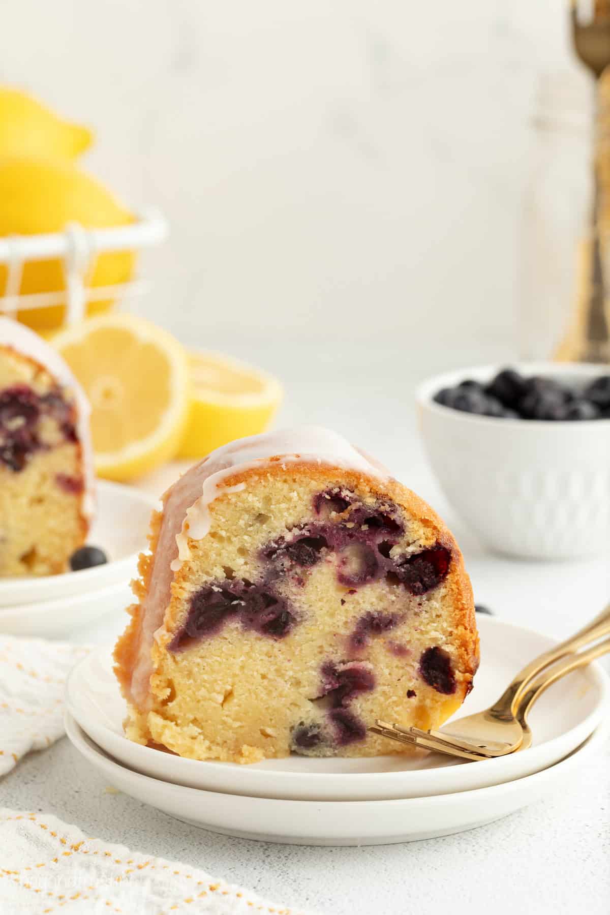 This easy lemon blueberry bundt cake recipe is a moist sour cream bundt cake bursting with fresh lemon and heaps of juicy blueberries. A slice of lemon blueberry bundt cake on a plate next to a fork.