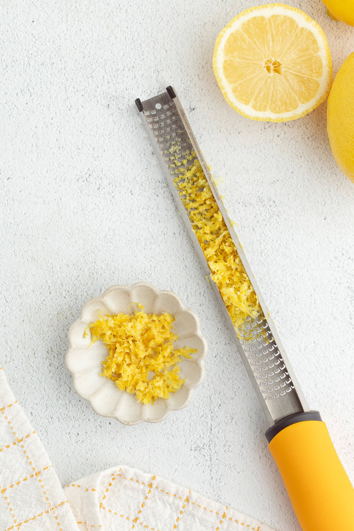 Overhead view of a citrus zester next to a small bowl of lemon zest.