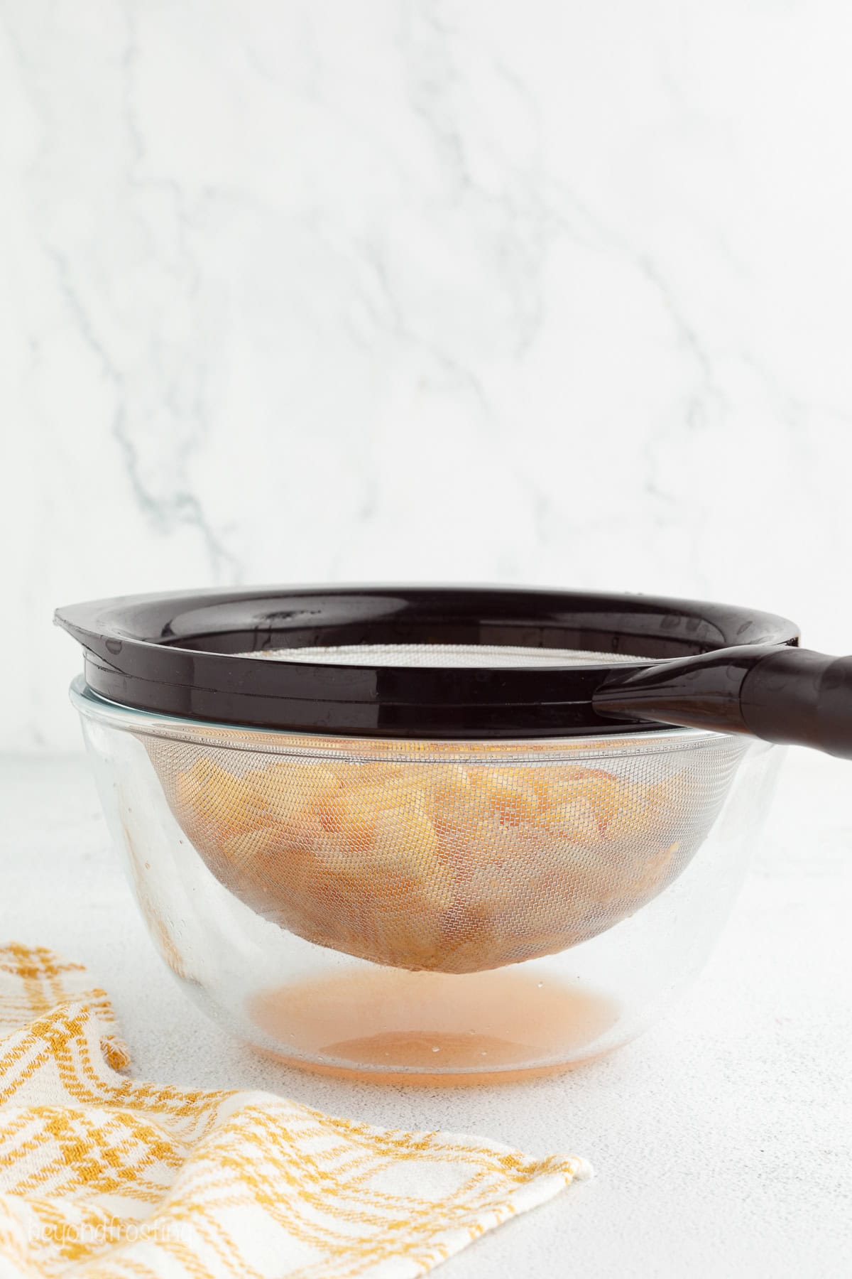 Diced peaches draining in a mesh strainer set over a bowl collecting the juice.