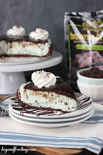 A slice of Brownie Brittle Grasshopper Pie on a plate in front of a full cake on a cake stand