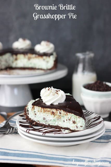 A slice of Brownie Batter Grasshopper Pie on a plate in front of the full cake on a cake stand