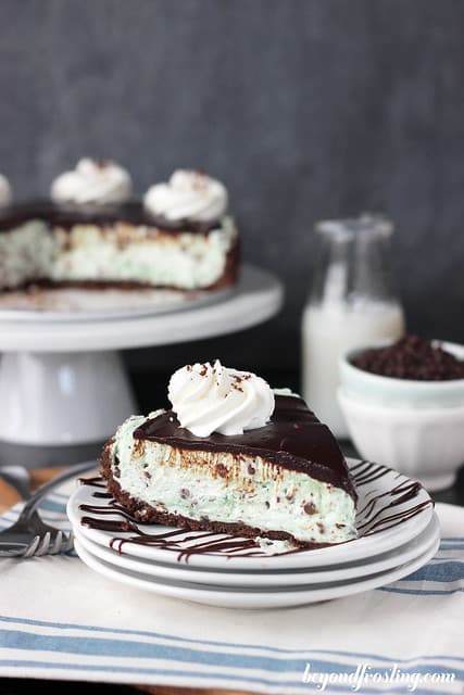 A slice of Brownie Brittle Grasshopper Pie on a plate with chocolate drizzle and a swirl of whipped cream