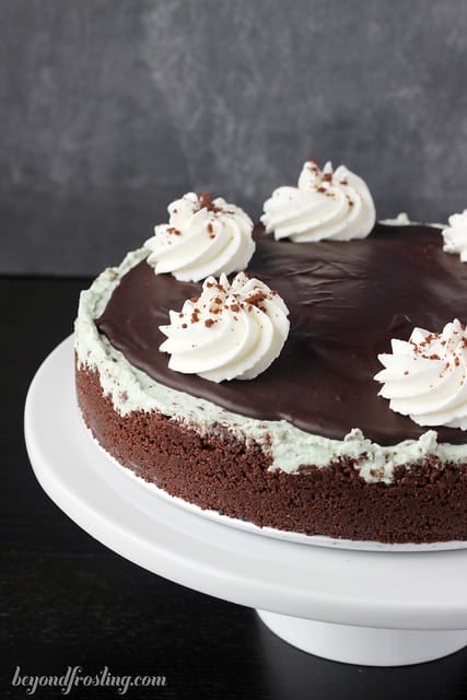 A whole Brownie Brittle Grasshopper Pie topped with swirls of whipped cream on a white cake stand
